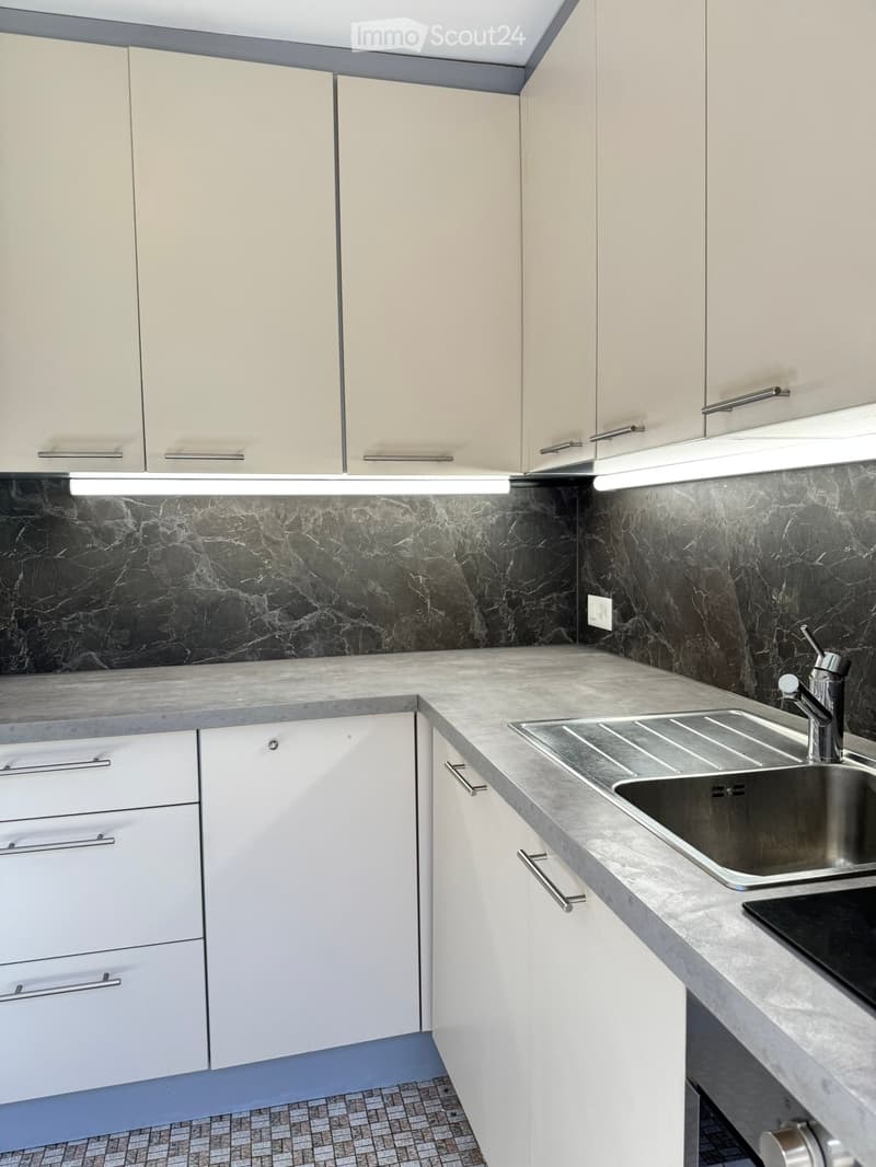 Modern kitchen with white cabinets, marble backsplash, and stainless steel sink.