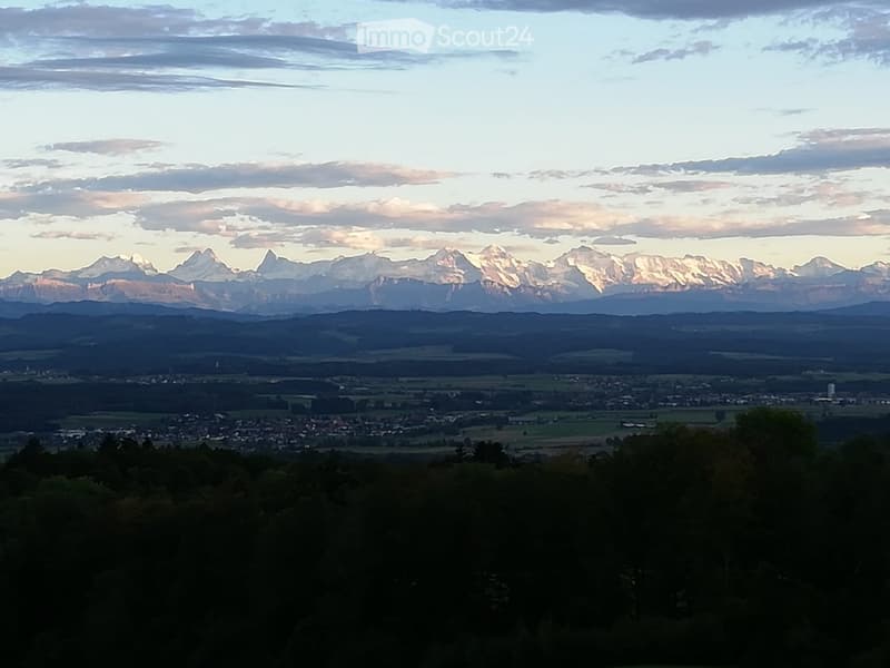 Panoramic view of a town nestled in a valley with distant mountain ranges under a partly cloudy sky.
