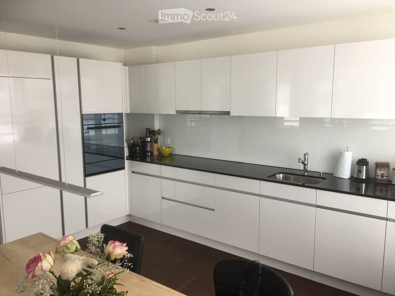 Modern kitchen with white cabinets, black countertops, and stainless steel appliances. Includes a sink, oven, and a small dining area with a table and chairs.