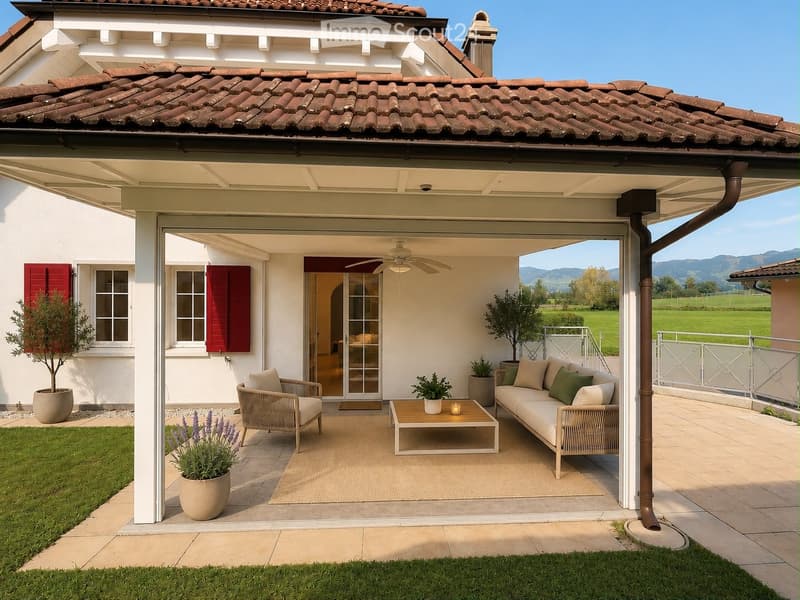 A covered outdoor patio area with a sofa, coffee table, and chairs, surrounded by potted plants and a scenic view of a green field and mountains.