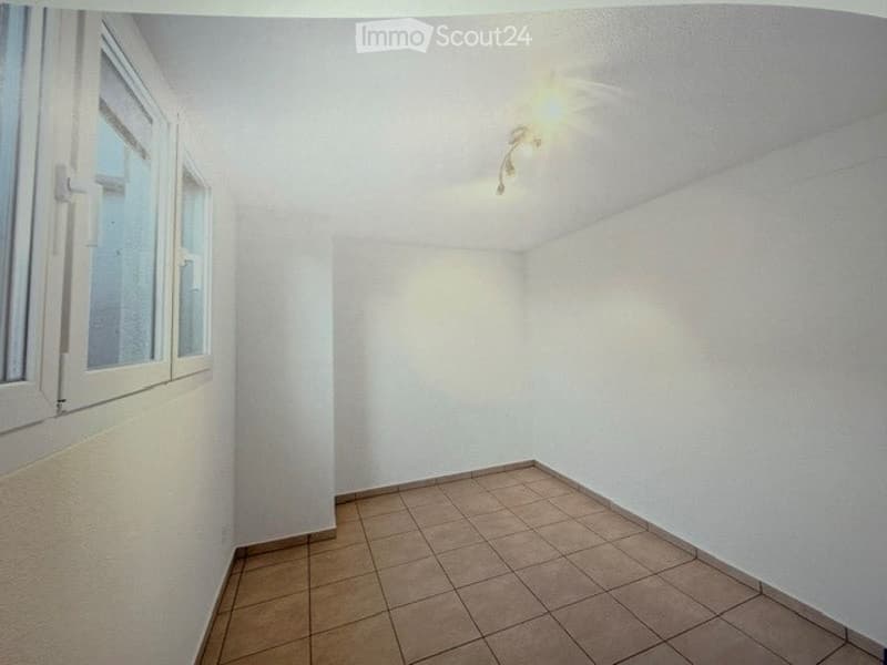 Empty room with tiled floor, white walls, and a single window with white frame. No furniture or equipment present.