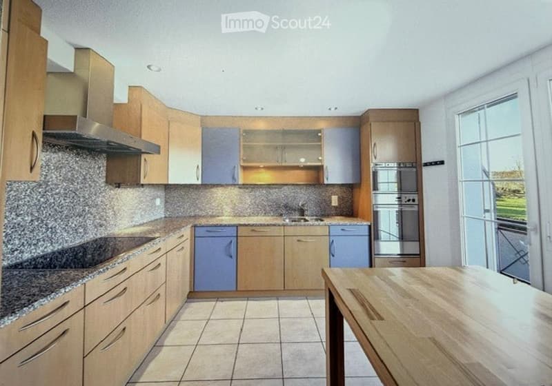 Modern kitchen with light wooden cabinets, stainless steel appliances, granite countertops, and a wooden dining table.