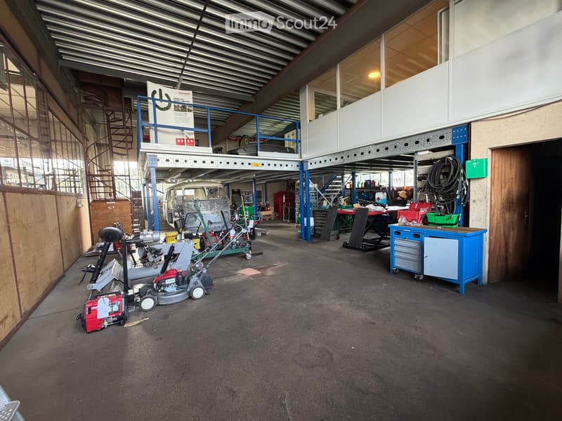 A spacious garage with a concrete floor, metal shelving, and various tools and equipment, including a lawn mower, workbench, and motorcycle.