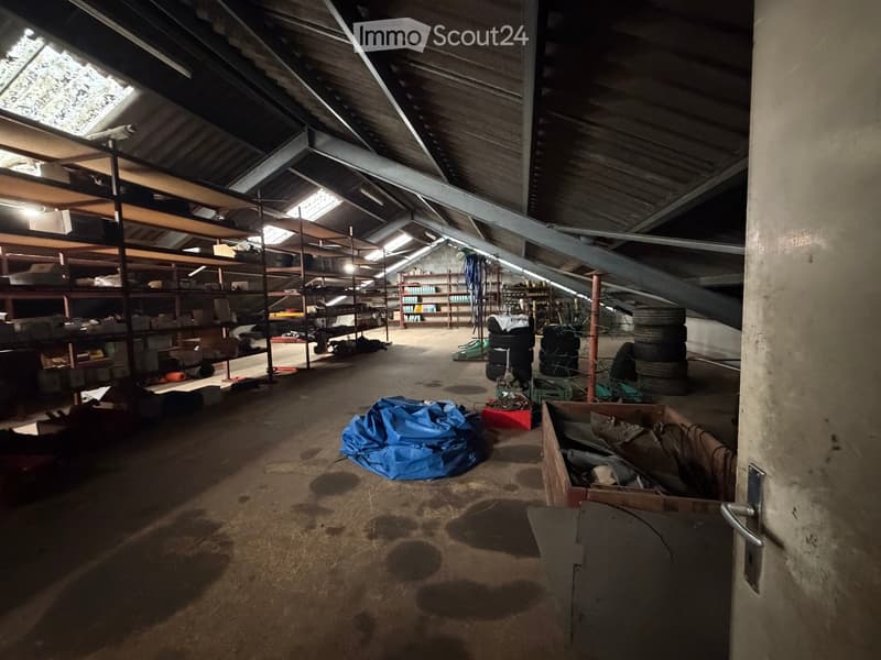 Empty attic space with exposed wooden beams, metal shelving units, and scattered storage items including tires, boxes, and tools.