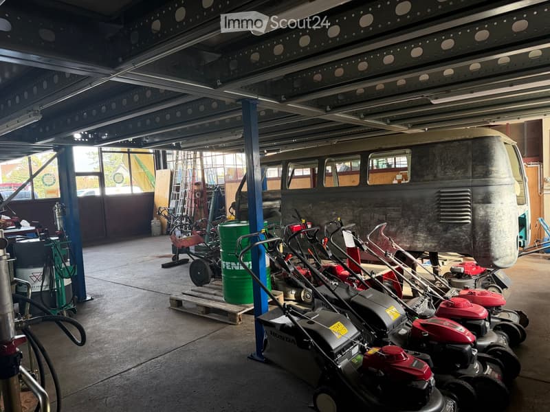 Garage with multiple lawnmowers, barrels, and a van, supported by metal beams and lighting.