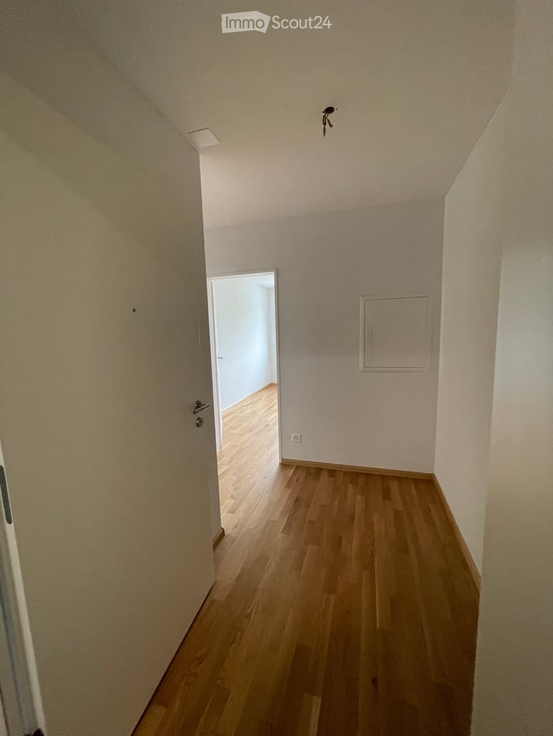 Empty hallway with wooden flooring, white walls, and a door leading to another room.