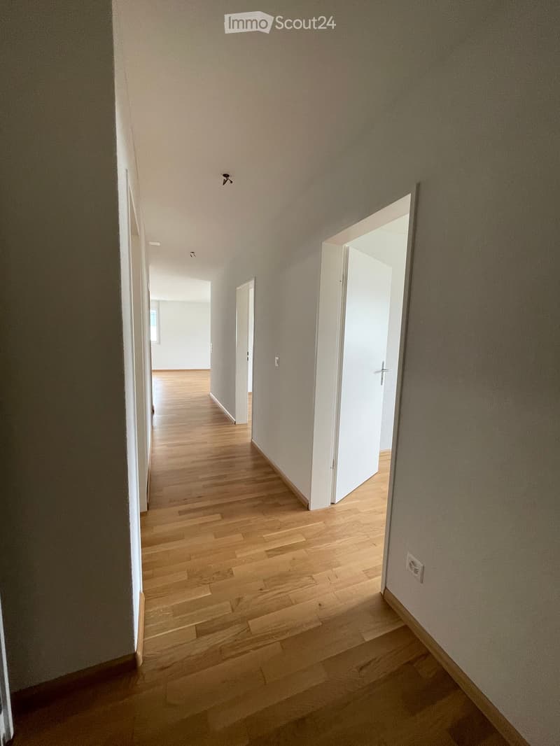 Empty hallway with wooden flooring, white walls, and open doors leading to other rooms.