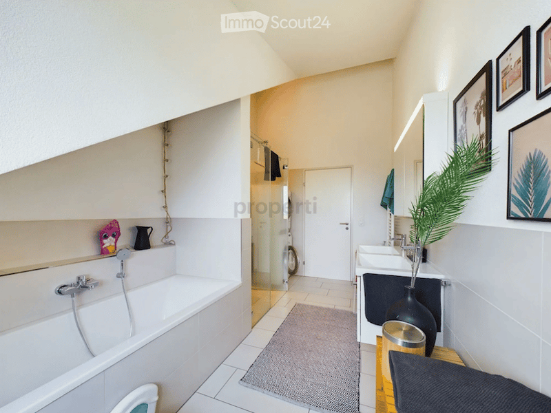 Modern bathroom with a bathtub, sink, and mirror. Includes a small plant in a vase, a stool, and picture frames on the wall.