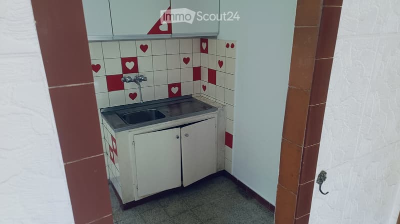 Small bathroom with a sink, faucet, and white cabinet. The walls are tiled with a red and white pattern featuring heart designs.