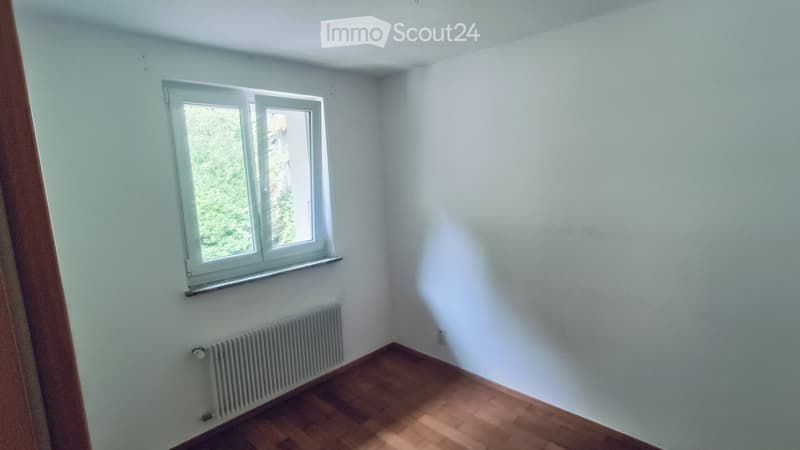 Empty room with light blue walls, wooden floor, white window, and radiator.
