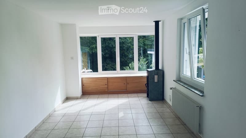 Empty room with tiled floor, white walls, large windows, built-in wooden cabinetry, and a wood-burning stove.
