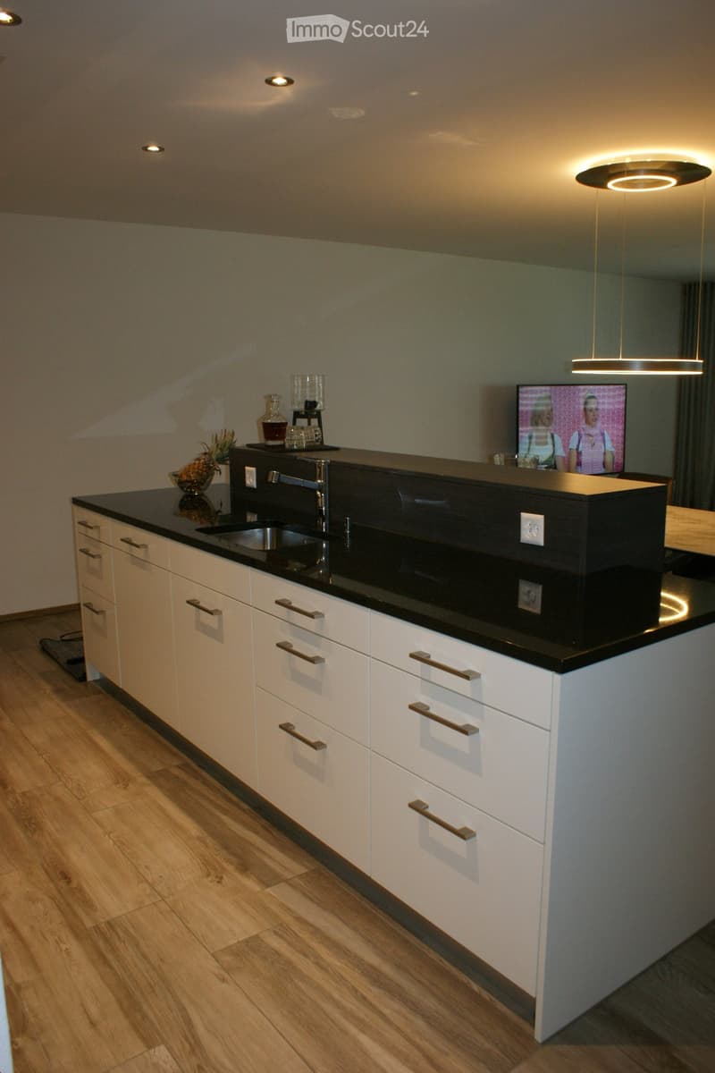 Modern kitchen with white cabinets, black countertops, and a central island. Features a sink, faucet, and decorative items on the counter.