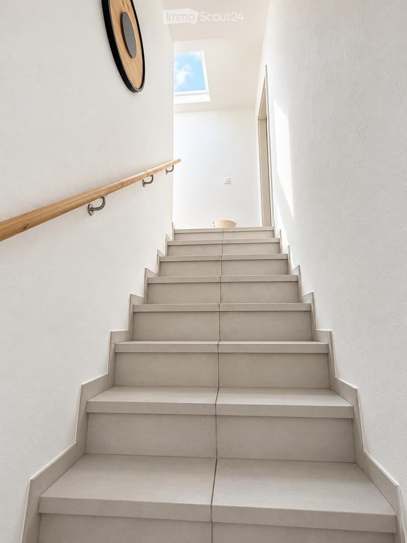 Modern staircase with light grey concrete steps, wooden handrail, white walls, and a skylight at the top.