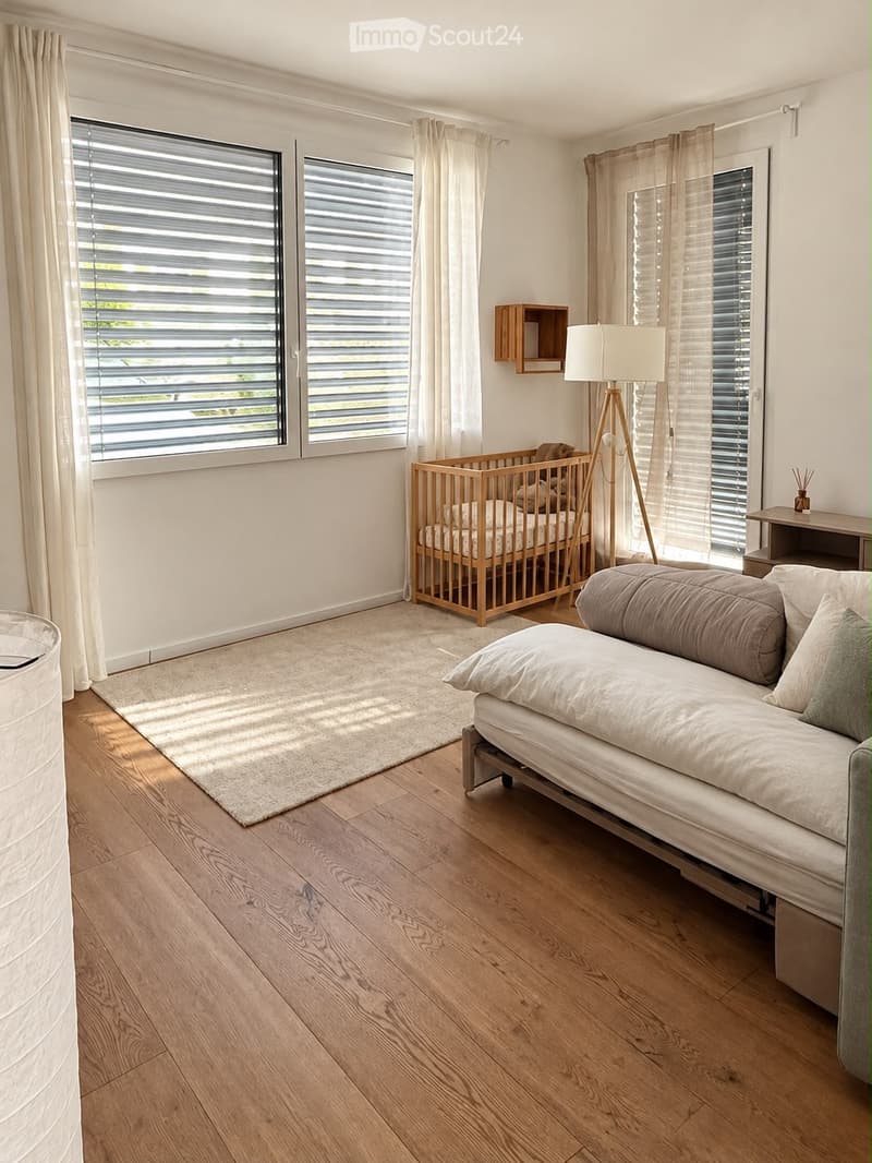 Bright bedroom with wooden flooring, large windows with blinds, a sofa, a wooden cradle, a floor lamp, a small shelf, and a side table.