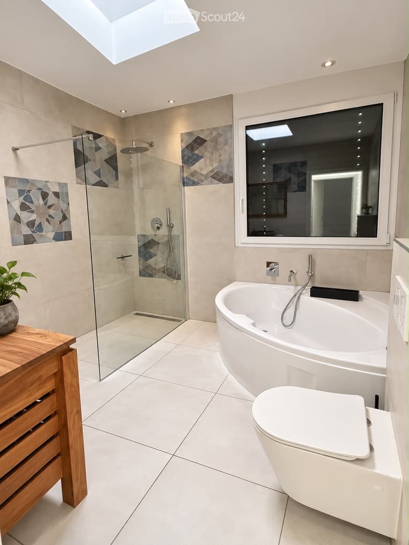 Modern bathroom with a large bathtub, toilet, glass-enclosed shower, and a wooden shelf with a plant. Features a skylight and large window.