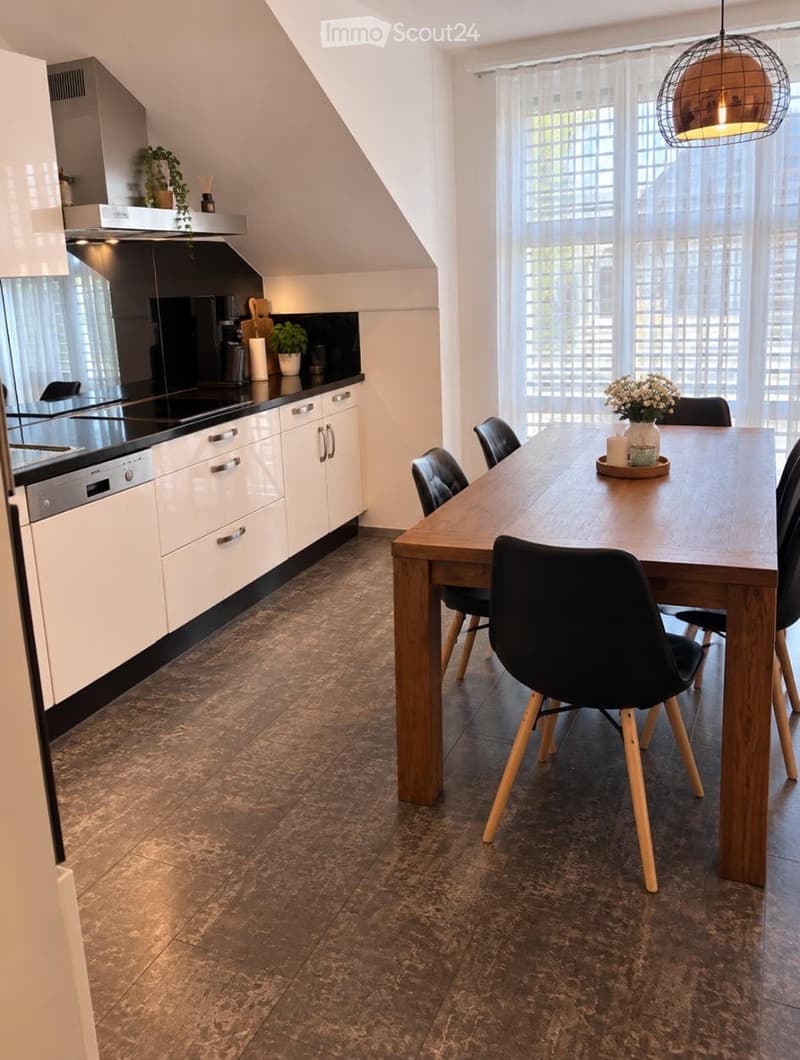 Modern kitchen with white cabinets, stainless steel appliances, a dining table with chairs, and a pendant light fixture.