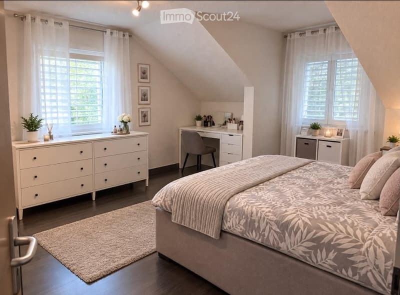 Cozy attic bedroom with slanted ceilings, large windows, a bed with patterned bedding, a nightstand, a desk with a chair, and a drawer unit. The room features a warm, inviting atmosphere with soft lighting and decorative plants.