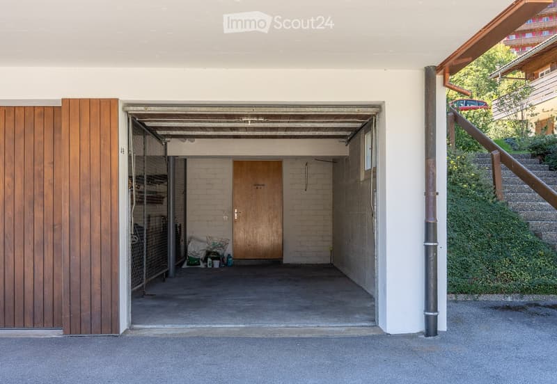 Garage entrance with wooden doors, concrete floor, and storage area visible inside.