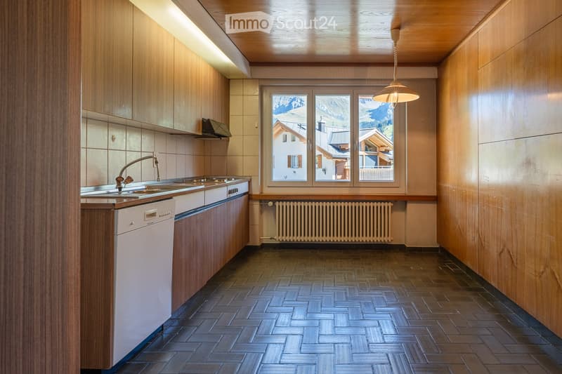 Modern kitchen with wooden cabinets, a sink, a dishwasher, and a radiator, featuring large windows with a scenic mountain view.