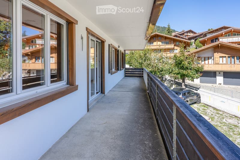 Balcony with wooden railings, large windows, and a view of neighboring houses and greenery.