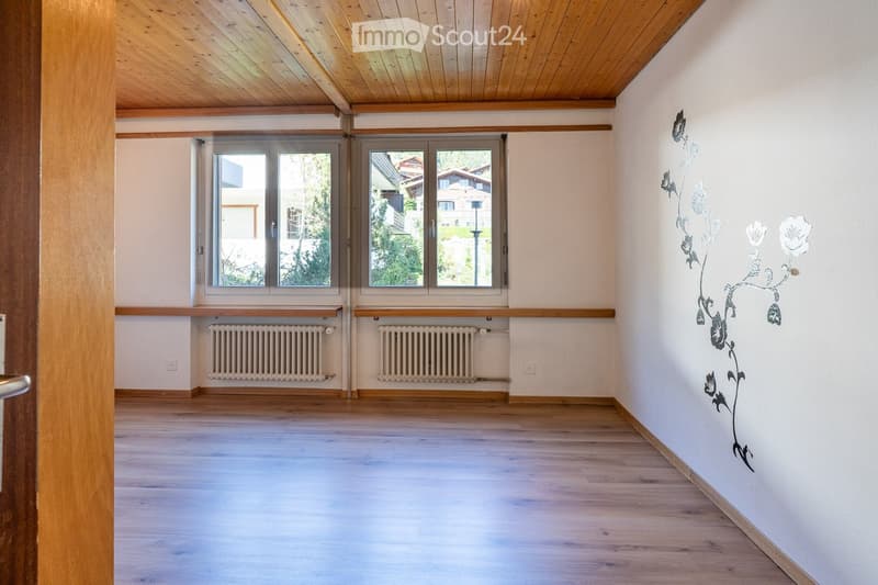 Empty room with wooden flooring, white walls, large windows, radiators, and a decorative wall sticker featuring a floral design.