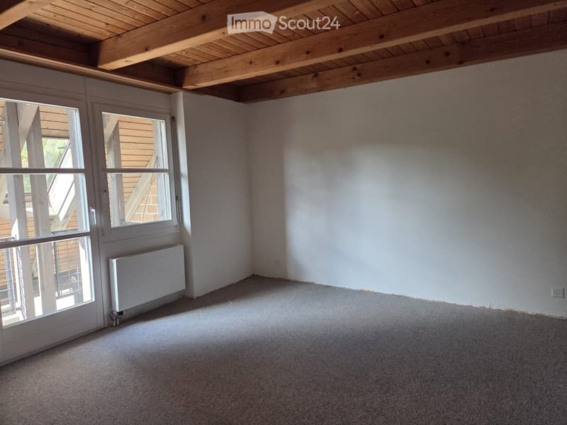 Empty room with exposed wooden beams on the ceiling, large windows, and a radiator on the wall.