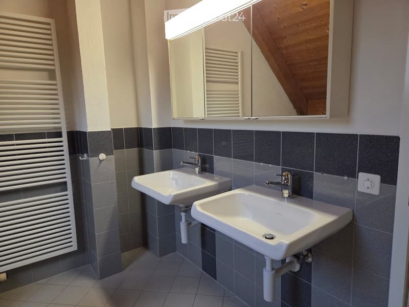 Modern bathroom with two white sinks, chrome faucets, dark grey tiles, and a white radiator.