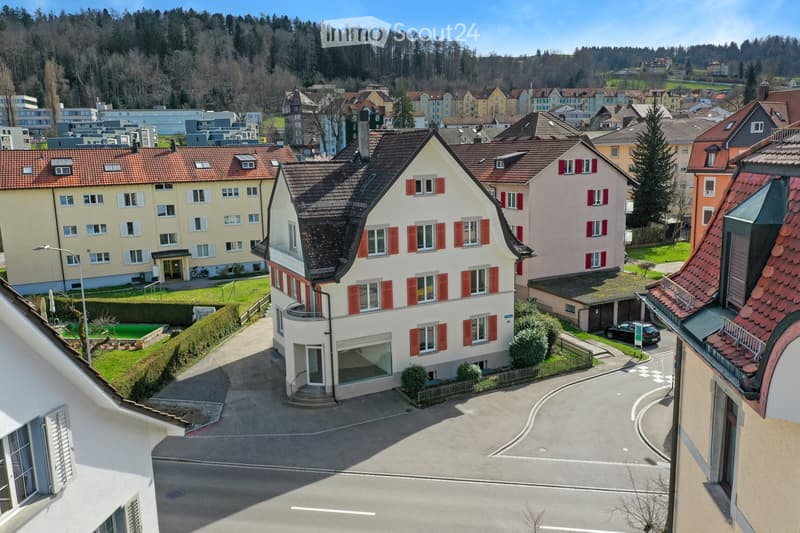 Aerial view of a residential area with multiple houses, red-tiled roofs, and surrounding greenery.