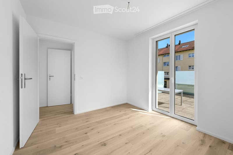 Empty room with light wooden flooring, white walls, and a large sliding glass door leading to a balcony. The room has a neutral, minimalist design with no furniture or decorations.