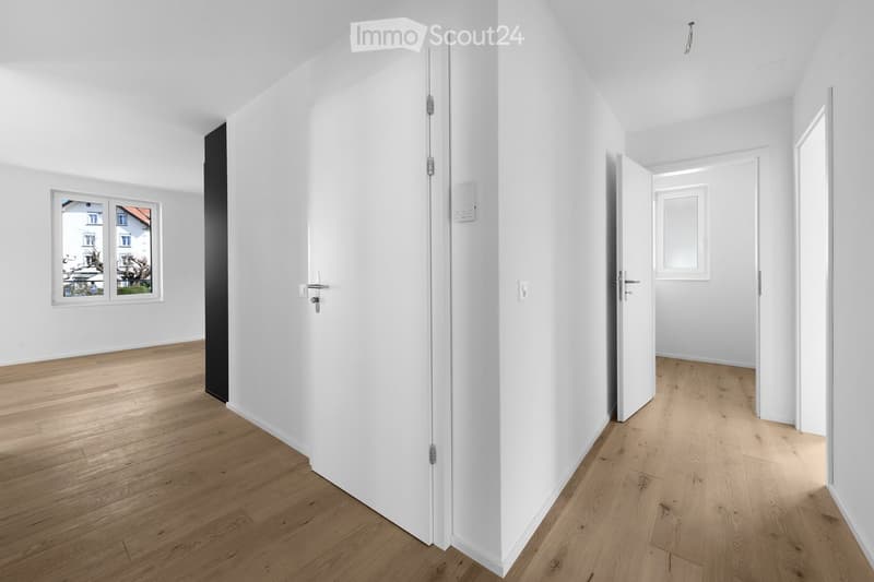 Empty hallway with white walls, wooden flooring, and multiple doors leading to other rooms.