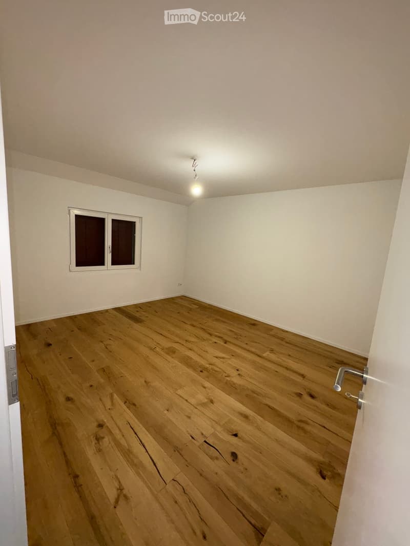 Empty room with wooden flooring and white walls, featuring a small window and a door.