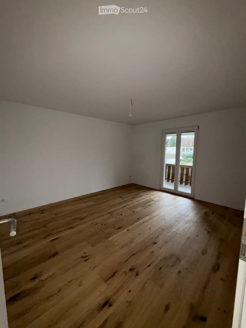 Empty room with wooden flooring, white walls, and a sliding glass door leading to a balcony.
