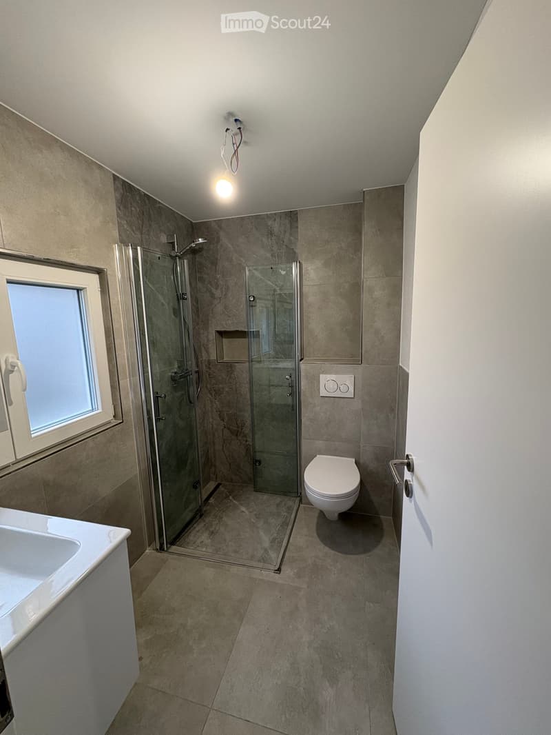 Modern bathroom with a glass-enclosed shower, toilet, bathtub, and a window providing natural light.