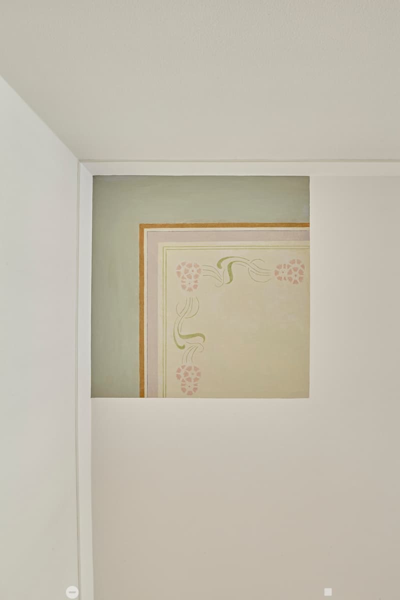 A framed artwork with floral and decorative design is displayed on a white wall in a room.