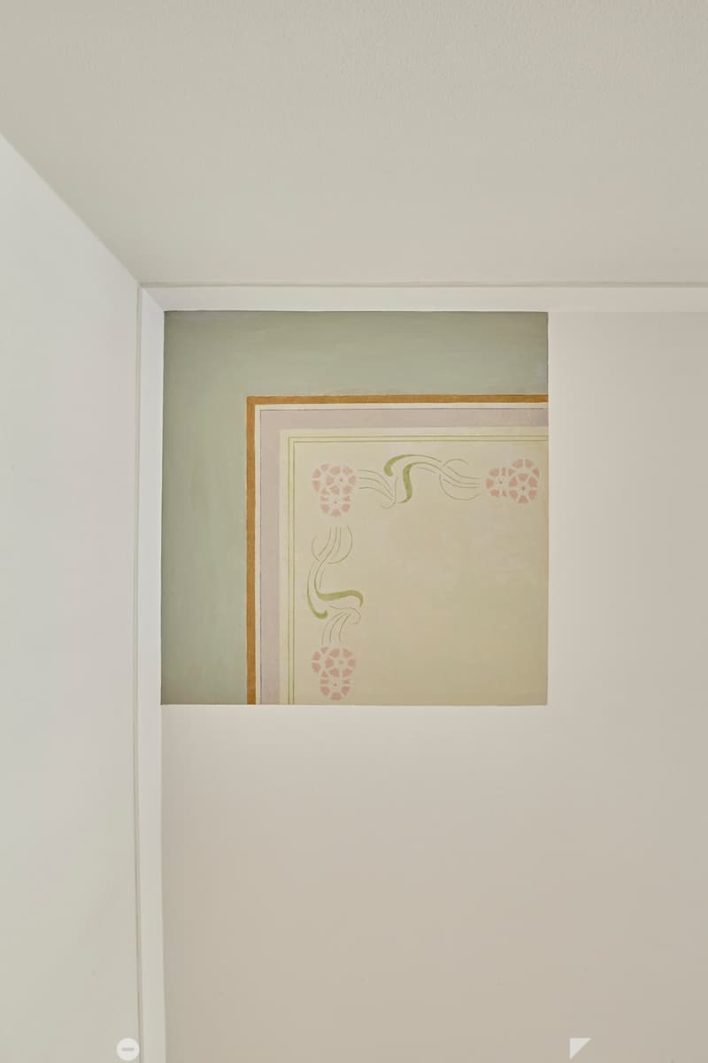 A framed artwork with floral and decorative design is displayed on a white wall in a room.