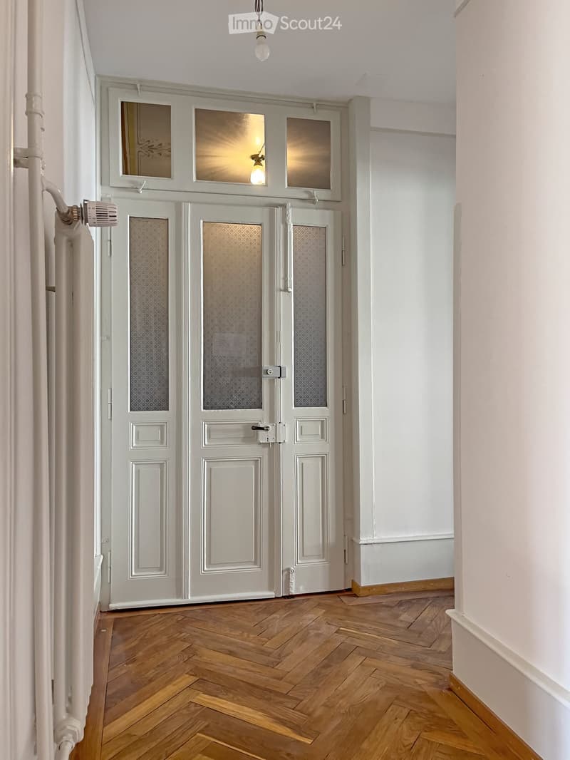 Hallway with wooden herringbone flooring, white walls, and double doors with frosted glass panels.