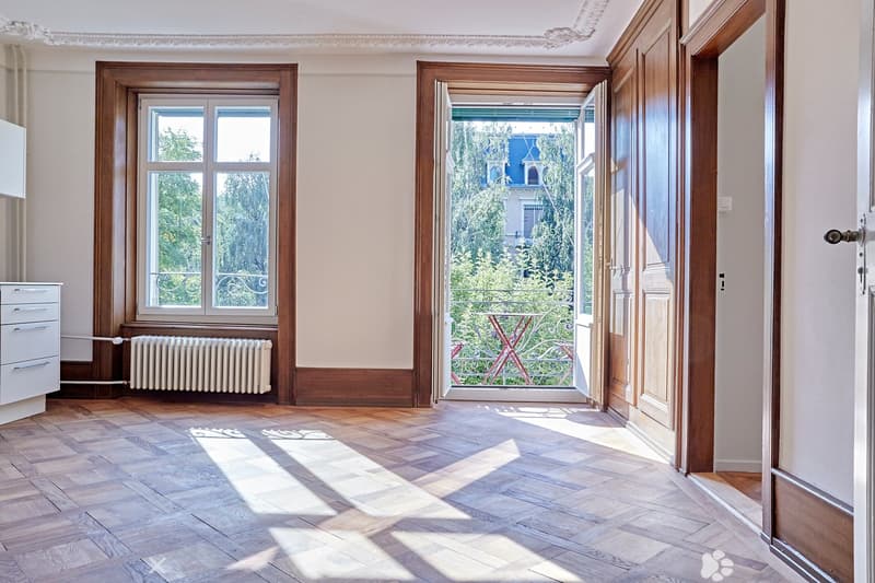 Empty hallway with wooden flooring, large windows, and an open door leading to a balcony area with outdoor furniture visible.
