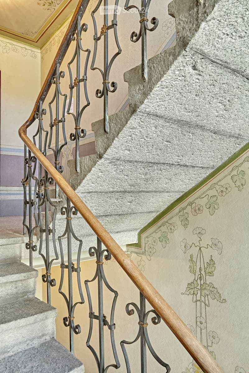Staircase with ornate metal railing and wooden handrail, featuring decorative floral wall art.