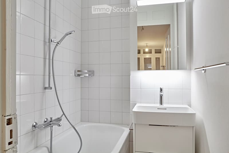 Modern bathroom with white tiled walls, a bathtub with a handheld showerhead, a sink with a modern faucet, and a large mirror above the sink.