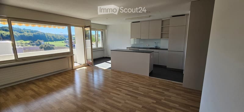 Bright, modern kitchen with wooden flooring, large windows offering a scenic view, and fitted cabinets.