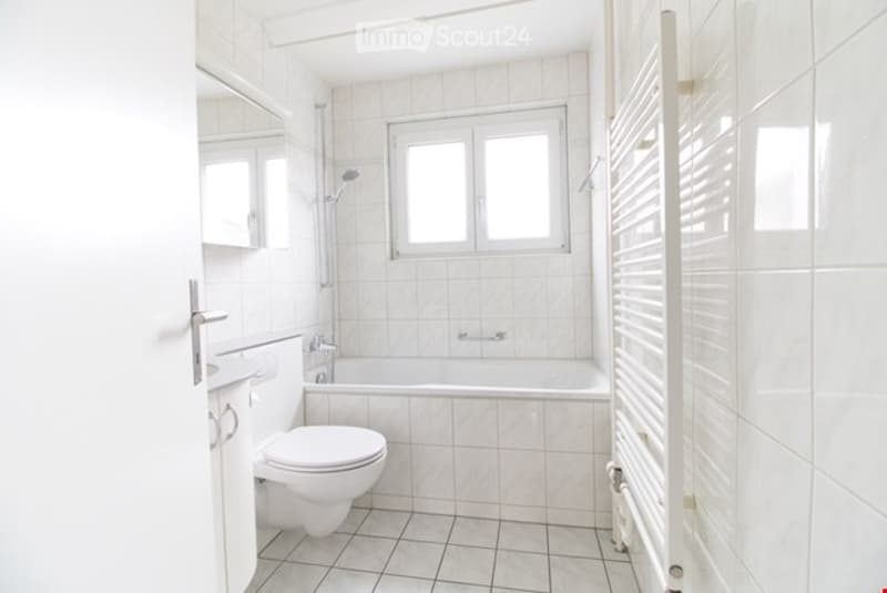Bathroom with white tiles, white toilet, bathtub, shower, sink, mirror, and radiator