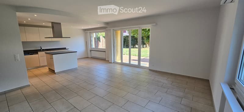 Empty kitchen with tiled floor, white cabinets, island, and large sliding glass doors leading to a garden view.
