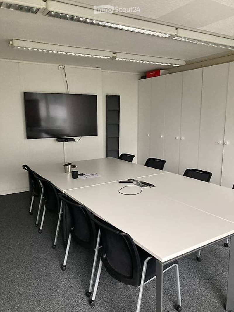 conference room, long table, black chairs, flatscreen TV mounted on wall, white walls, gray carpet, white cabinets, ceiling lights