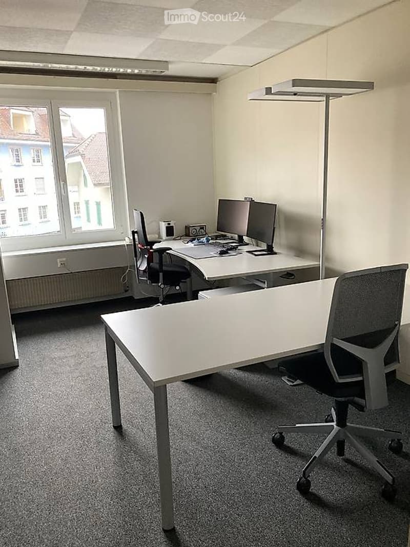 Empty office room with desk, chairs, monitors, and window.