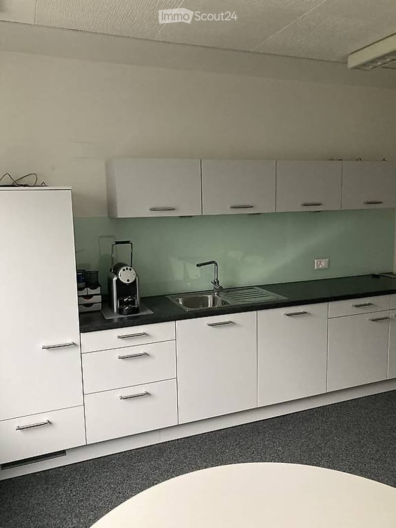 modern and minimalistic kitchen with white cabinets, green splashback, black countertop, stainless steel sink, modern faucet, round table