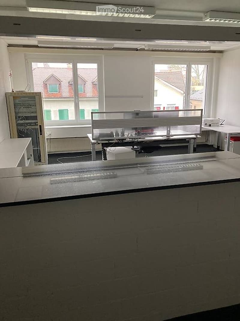 Large room with white walls, a central desk, large windows, and mounted equipment.