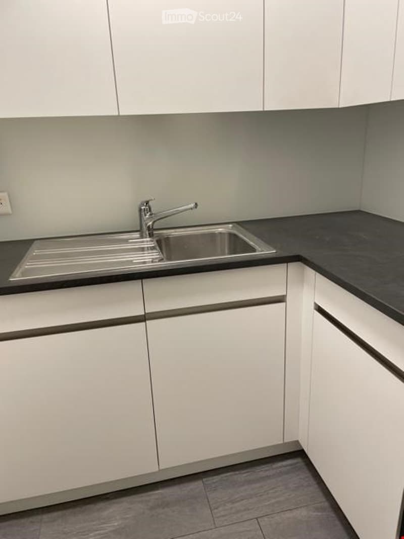 Modern kitchen with white cabinets, black countertops, and a stainless steel sink.