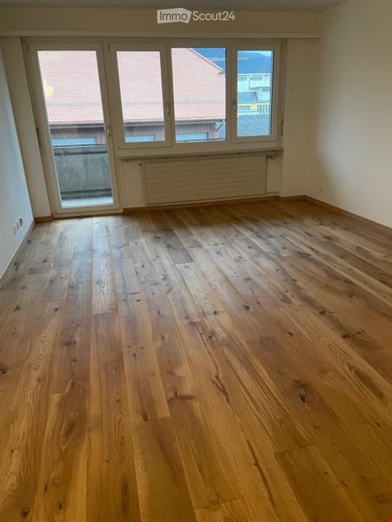 Empty room with wooden flooring, large windows, and white walls. No furniture or equipment present.