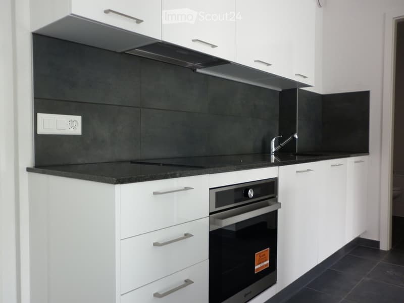 Modern kitchen with white cabinets, black countertops, and built-in oven. Features sleek design with stainless steel fixtures and a black backsplash.