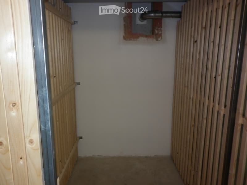 Empty hallway with unfinished wooden paneling on both sides, a metal door frame on the left, and a partially visible pipe in the ceiling.